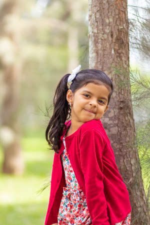 Little girl in flower dress and red sweater, very happy and smiling in the forestの写真素材