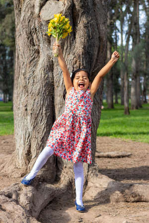 Little girl in dress celebrating in the park with a bouquet of flowers in her handの写真素材