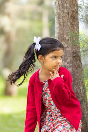 Little girl in flower dress and red sweater, very happy and smiling in the forestの写真素材