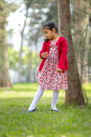 Little girl in flower dress and red sweater, very happy and smiling in the forestの写真素材