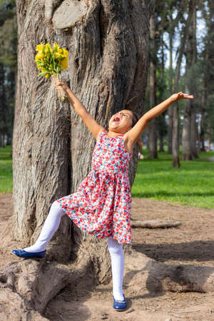 Little girl in dress celebrating in the park with a bouquet of flowers in her handの写真素材