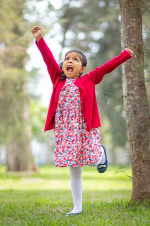 Little girl in flower dress and red sweater, very happy and smiling in the forestの写真素材