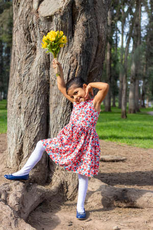 Little girl in dress celebrating in the park with a bouquet of flowers in her handの写真素材