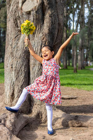Little girl in dress celebrating in the park with a bouquet of flowers in her handの写真素材