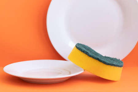 Yellow sponge next to white plate with orange backgroundの写真素材