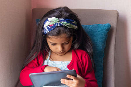 Little girl sitting is playing with her tablet at homeの写真素材