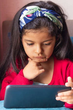 Little girl sitting is playing with her tablet at homeの写真素材