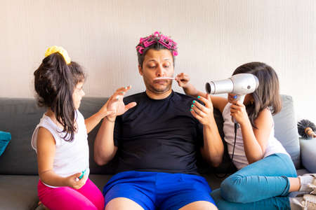Pretty daughters are painting the nails and combing the hair of their handsome young fatherの写真素材
