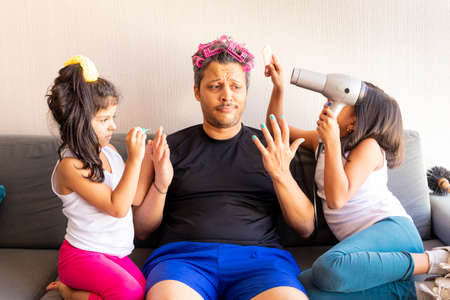 Pretty daughters are painting the nails and combing the hair of their handsome young fatherの写真素材