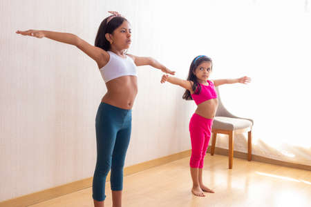 Two little sisters are doing exercise routines in the living room at homeの写真素材