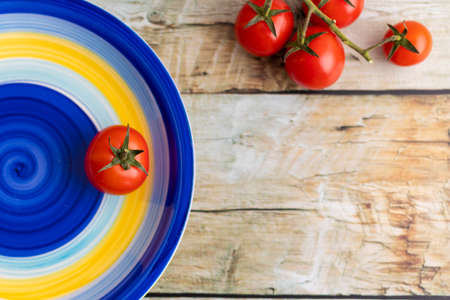 Cherry tomatoes on colorful striped plate and brown wooden backgroundの写真素材