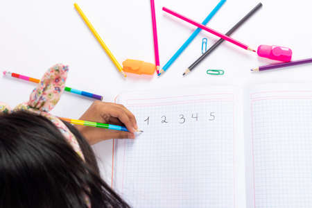 Cute left-handed girl is writing with a pencil in her notebook.