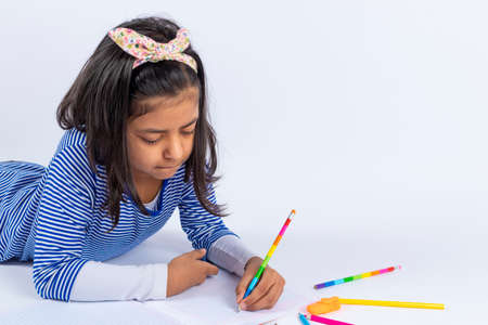 Cute left-handed girl is writing with a pencil in her notebook.