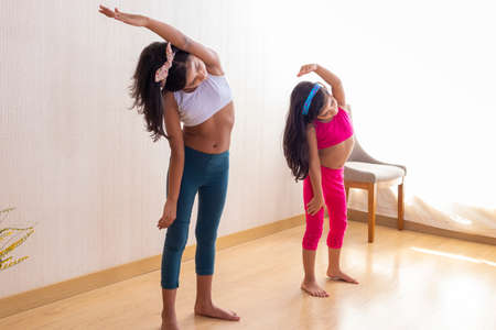 Two little sisters are doing exercise routines in the living room at homeの写真素材