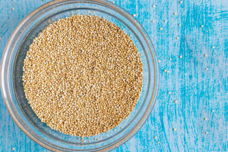 Raw quinoa grains inside transparent bowl, on blue tableの写真素材