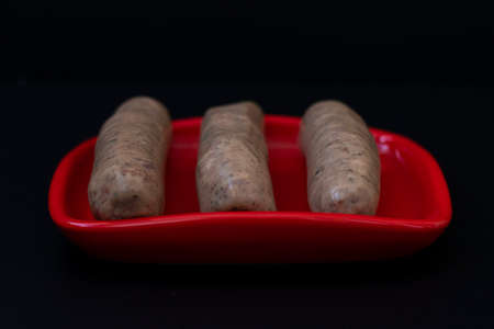Raw sausages on red bowl on dark backgroundの写真素材