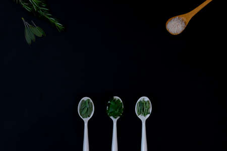 White spoons with herbs spices for cooking. On black background with copy spaceの写真素材