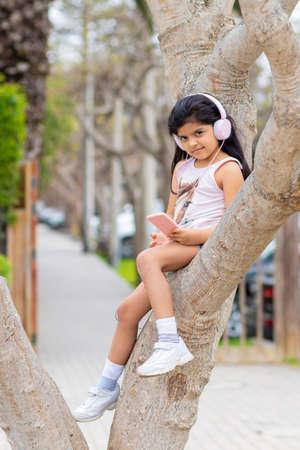 Little girl is listening to music with her headphones on a treeの写真素材