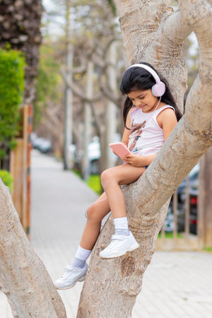 Little girl is listening to music with her headphones on a treeの写真素材