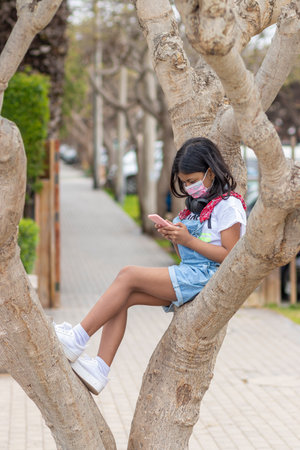 Little girl is listening to music with her headphones on a treeの写真素材