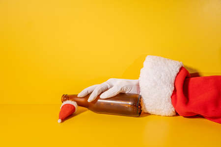 Santa Claus holding beer bottle with his hands on yellow background