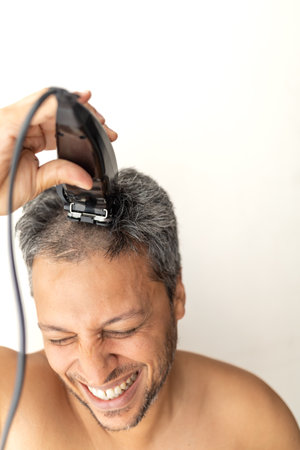 Handsome gray-haired man is cutting hair himself with an electric hair clipper.の写真素材