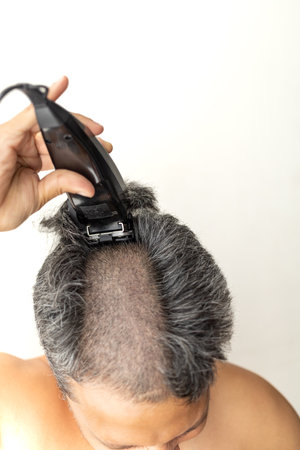 Handsome gray-haired man is cutting hair himself with an electric hair clipper.の写真素材