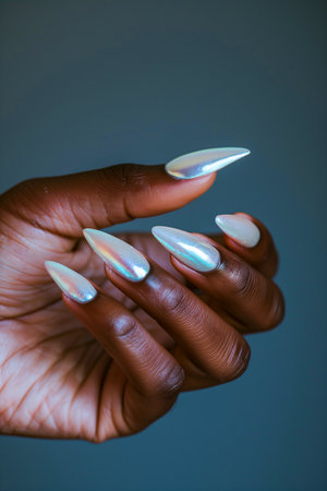 A hand holding a manicured set of long, pointed fingernails. The nails are painted white and have a glittery, iridescent finish. Concept of elegance and sophisticationの素材