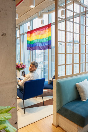 Senior man sitting in armchair with lgbt flag in cafeの写真素材