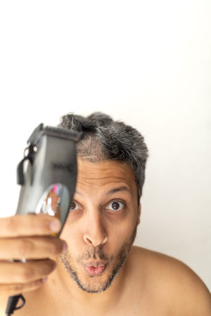 Gray-haired man is cutting hair himself with an electric hair clipper.の写真素材
