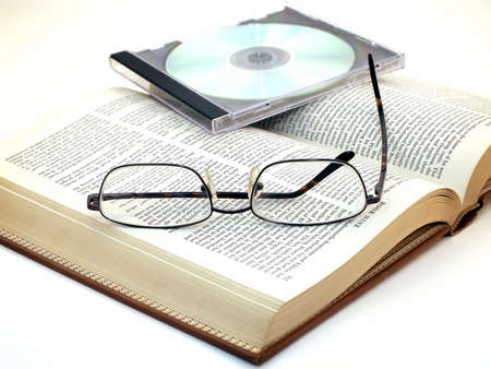 Pair of glasses rest on open book with CD on top.の写真素材
