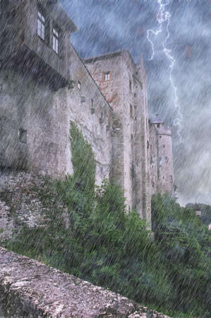 Rainy scene of massive castle walls with lightning in cloudy sky.の写真素材