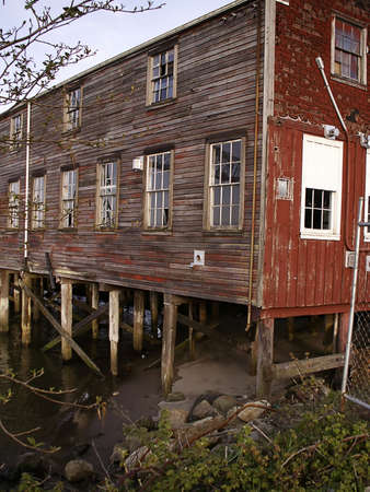 Old waterfront mill stands on pilings at dusk.の写真素材