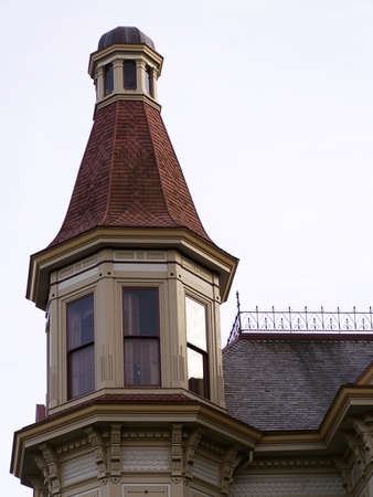 Vintage Victorian turret tower with red shingle roof stands starkly against the afternoon sky.の写真素材