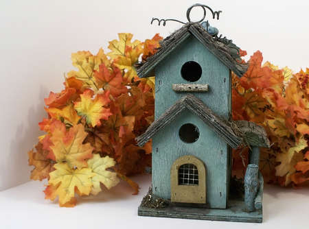 Weathered green birdhouse nestled in orange fall leaves.の写真素材
