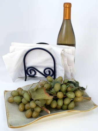 Plate of green grapes with white cloth napkins and bottle of white wine on neutral background.の写真素材