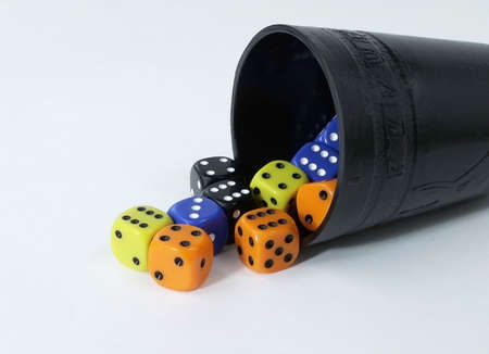 Black dice cup with multi-colored dice spilling out onto white background.の写真素材
