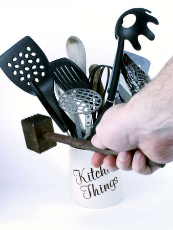 Man's hand grasps wooden meat tenderizer, with kitchen utensils in background.の写真素材