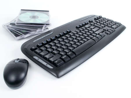 Black wireless keyboard and mouse with stack of CDs in cases, isolated on white background.の写真素材