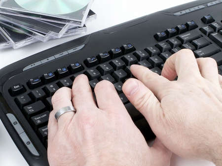 Male hands typing on black keyboard with stack of CDs behind, isolated on white background.の写真素材
