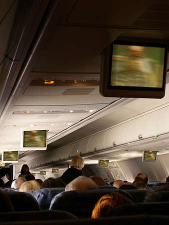 Stewardess serves passengers aboard jetliner as move plays on overhead monitors in cabin.の写真素材