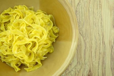 Close up big yellow noodle scald in brown bowl with wood background.の写真素材