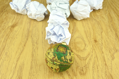 Paper ball place direct to the globe meaning major waste problems on wood background.の写真素材