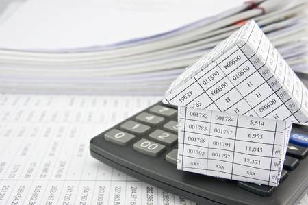 House on calculator place on finance account with pile of paperwork as background.の写真素材