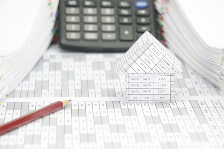 Brown pencil and house on finance account have blur calculator with pile of document as background.の写真素材