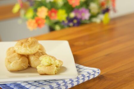 Eclair cream overflow place in plate with blue fabric on wood table and blur flower as background.の写真素材