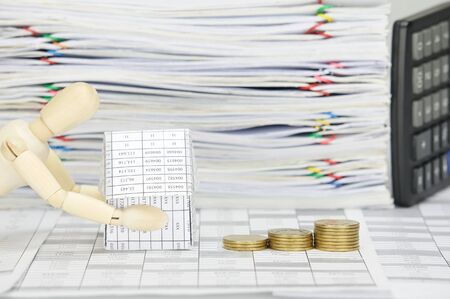 Wooden dummy holding house and step pile of gold coins on finance account have blur calculator place...