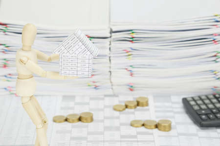 Wooden dummy holding house on finance account have blur calculator and step pile of gold coins with...