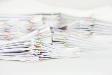Pile paperwork of report with colorful paperclip on white table have blur pile overload document as...