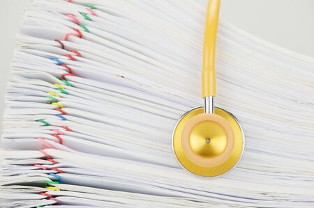 Yellow and gold stethoscope have blur pile paperwork of report with colorful paperclip as background.の写真素材